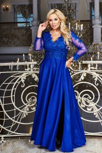 Krásna blondínka v modrých šatách s flitrovaným živôtikom a dlhými sieťovinovými rukávmi na poschodí luxusnej miestnosti s vytepaným balkónom 