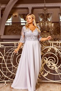 Krásna blondínka v luxusnej miestnosti na poschodí s tvarovaným zabradlím v nádherných sivých šatách s fltrovaným živôtikom a dlhou sukňou
