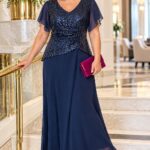 Plus size žena v tmavomodrých spoločenských šatách s flitrovaným živôtikom a šifónovou sukňou, s cyklámenovou listovou kabelkou a lodičkami.