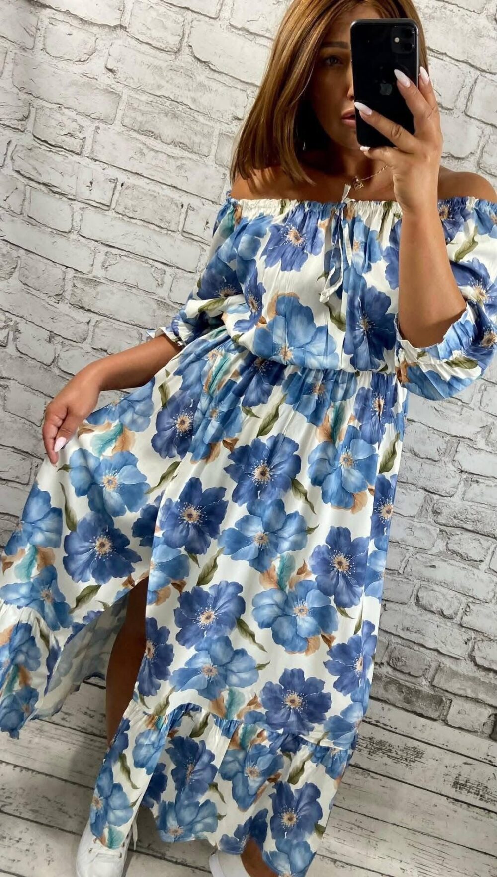 Žena v dlhých šatách s modrou kvetinovou potlačou, s odhalenými ramenami a rozparkom