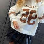 Biela mikina s karamelovým nápisom Los Angeles 95 a pruhmi na rukávoch, dĺžka 76 cm.