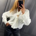 Biela elegantná blúzka pre moletky so šálovým výstrihom a zlatou kovovou ozdobou.