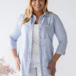 Dámska plus size bavlnená blúzka s jemnými modrými pásikmi, 3/4 rukávmi a voľnejším strihom, kombinovaná s bielymi nohavicami.