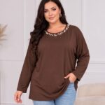 Hnedá dámska tunika vo voľnom strihu s dlhými rukávmi a okrúhlym výstrihom zdobeným bielymi perlami rôznych veľkostí. Plus size modelka ju kombinuje so svetlomodrými rifľami.