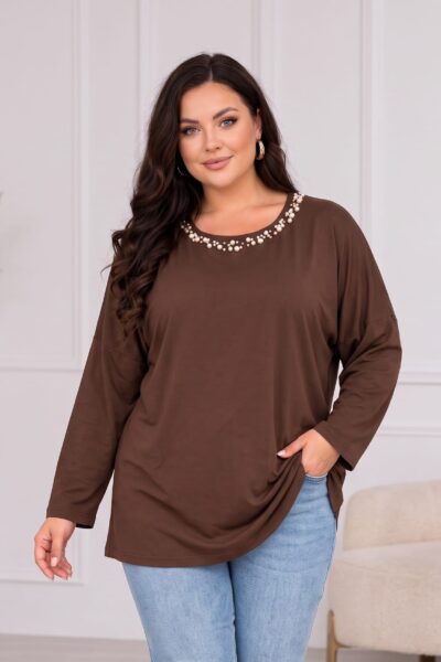 Hnedá dámska tunika vo voľnom strihu s dlhými rukávmi a okrúhlym výstrihom zdobeným bielymi perlami rôznych veľkostí. Plus size modelka ju kombinuje so svetlomodrými rifľami.