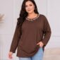Hnedá dámska tunika vo voľnom strihu s dlhými rukávmi a okrúhlym výstrihom zdobeným bielymi perlami rôznych veľkostí. Plus size modelka ju kombinuje so svetlomodrými rifľami.
