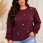 Fialová dámska plus size mikina v tmavom slivkovom odtieni, zdobená výraznými zlatými srdiečkami a drobnými zlatými ozdobami. Má okrúhly výstrih, voľnejší strih a dlhé nazberané rukávy zakončené manžetami.