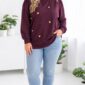 Usmievavá plus size žena vo fialovej mikine so zlatými plastickými srdiečkami a drobnými cvočkami, svetlomodrých džínsoch a čiernych mokasínach v svetlom elegantnom interiéri.
