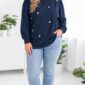 Plus size modelka v tmavomodrej mikine so zlatými plastickými srdiečkami a drobnými cvočkami, s jemne nariasenými rukávmi, svetlomodrými džínsami a čiernymi mokasínami v modernom bielom interiéri.