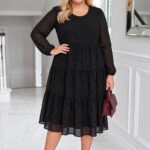 Usmiata blondína plnšej postavy stojí v svetlom elegantnom interiéri pri okne. Má na sebe čierne midi šaty s jemnými drobnými bodkami, priehľadnými dlhými rukávmi a trojstupňovou sukňou pod kolená. Jednu ruku má vbok, v druhej drží bordovú kabelku a obuté má bordové lodičky.