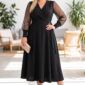 Plus size blondínka v elegantných čiernych midi šatách so zavinovacím výstrihom, priehľadnými rukávmi a opaskom s kovovou prackou. Outfit dopĺňajú saténové lodičky a kabelka vo farbe champagne.