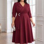 Plus size brunetka v elegantných bordových midi šatách s prekladaným živôtikom, striebornou prackou a rozšírenou sukňou v svetlom interiéri.