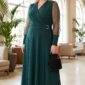 Plus size blondínka v elegantných smaragdovozelených midi šatách so zavinovacím výstrihom, priehľadnými rukávmi a opaskom so zlatou kovovou prackou. Outfit dopĺňajú čierne lodičky a malá čierna kabelka.