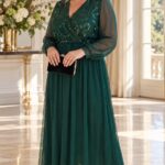 Plus size modelka v dlhých smaragdovozelených šatách s flitrovým zdobením na živôtiku, prekladaným výstrihom, priehľadnými šifónovými rukávmi a splývavou sukňou. Outfit dopĺňajú zlaté lodičky a čierna listová kabelka.