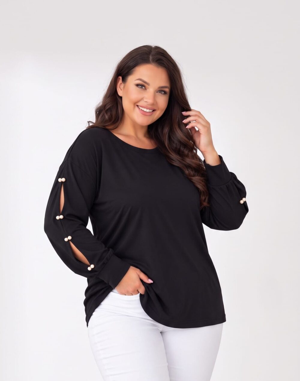 Čierna dámska plus size tunika s okrúhlym výstrihom a dlhými rukávmi s rozparkami zdobenými bielymi perlami. Detail tuniky na modelke v bielych nohaviciach.