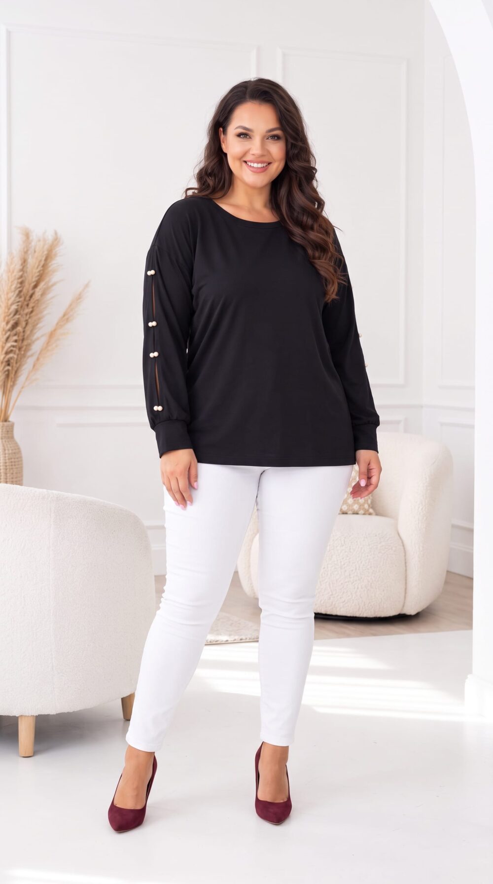 Čierna dámska tunika vo voľnom strihu s dlhými rukávmi, ozdobnými rozparkami a bielymi perlami. Plus size modelka v bielych nohaviciach a bordových lodičkách, celá postava.