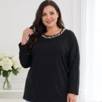 Plus size žena v čiernej tunike voľného strihu s dlhými rukávmi a okrúhlym výstrihom zdobeným bielymi perličkami. Detail tuniky v kombinácii so svetlomodrými rifľami.