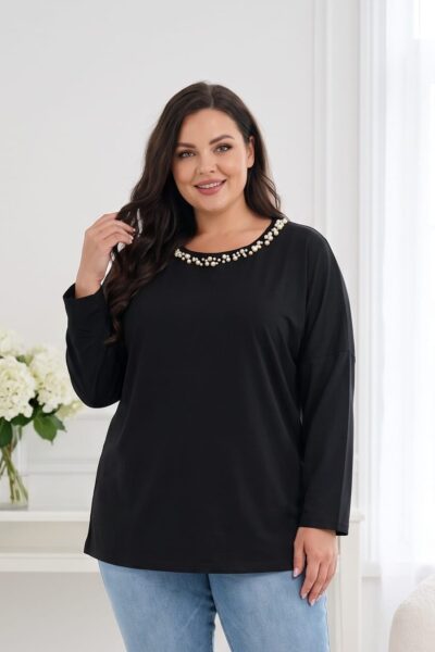 Plus size žena v čiernej tunike voľného strihu s dlhými rukávmi a okrúhlym výstrihom zdobeným bielymi perličkami. Detail tuniky v kombinácii so svetlomodrými rifľami.