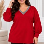 Plus size modelka v červenej tunike s voľným strihom, striebristosivým lemovaním V-výstrihu a dlhými balónovými rukávmi zakončenými manžetami. Tuniku dopĺňajú čierne nohavice. Modelka stojí vo svetlom elegantnom interiéri.
