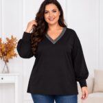 Plus size modelka v čiernej tunike s trblietavým strieborno-sivým V-výstrihom, balónovými rukávmi a širokými manžetami. Tuniku kombinuje s modrými rifľami.